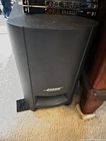 Front view of Bose Acoustimass subwoofer with logo visible, DVDs stacked on top