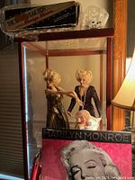 Overall view of display case containing three Marilyn Monroe dolls, photo book, and doll box