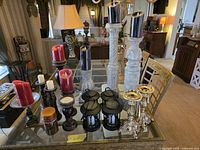 Full lot view on glass table showing candlesticks, pillar stands, lanterns, assorted candles