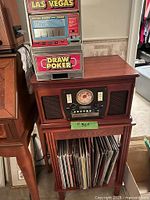 Record player console with vinyl LPs on lower shelf and slot machine on top