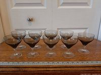 Front view of all eight smoke-grey champagne coupes aligned on wooden surface