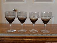 Four smoke-grey cordial glasses aligned, front view with ruler for scale