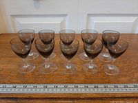 Ten smoke-grey sherry glasses aligned in two rows with ruler for scale