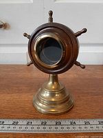 Front view of brass and wood ship wheel picture frame with ruler for scale