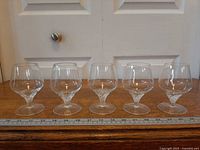 Front view of five crystal cognac glasses lined up with ruler for scale
