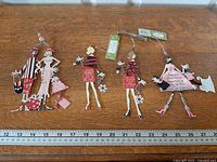 Four lady-shaped metal ornaments on tabletop with ruler for scale