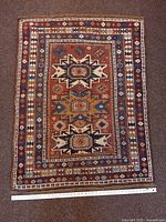 Full view of antique Lesghi rug on floor with ruler for scale