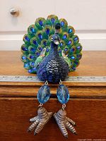 Front view of resin peacock showing tail, body texture, dangling legs with blue beads