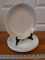 Stack of six Corelle Apricot Grove dinner plates with one displayed on stand, ruler shows size