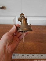 Side view of brass bell on anchor bracket held in hand