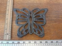 Front view of cast iron butterfly trivet beside ruler showing width ~6.75 in