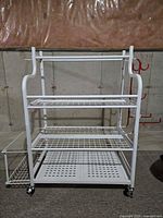 Front view of white metal storage rack with three wire shelves, side basket, casters visible