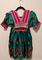 Front view of green floral Afghan-style child dress on hanger