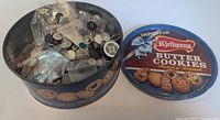 Overview of open Kjeldsens tin filled with mixed buttons and small resealable bags