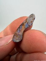 Front view of rough opal specimen held between fingers