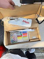 Box opened showing Handy Stitch handheld sewing machine and accessory kit