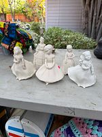 Group shot of five white porcelain girl figurines on shelf
