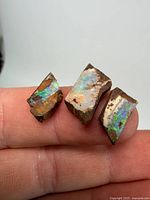 Three rough fire opal stones on fingertip showing colour flashes