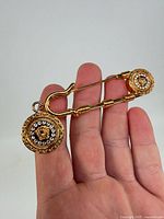 Full view of gold-tone safety pin brooch held in hand