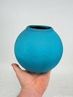 Front view of spherical turquoise blue vase held in hand