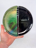 Front of round fused glass plate showing two-tone iridescent green and black design with white stripe
