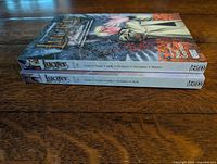 Side view of both books stacked showing spines with titles and volume numbers