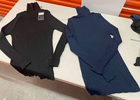 Black and navy ribbed turtleneck sweaters laid flat on table