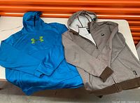 Burton brown heather zip hoodie and Under Armour blue pullover hoodie laid flat on table