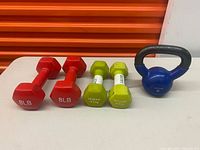 Full lot showing two red 8 lb dumbbells, two green GoZone 2.3 kg dumbbells, blue kettlebell