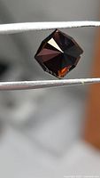 Front view of faceted cognac orange tourmaline held by tweezers