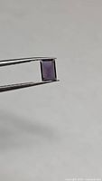 Loose bright purple rectangular gemstone held by tweezers