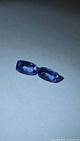 Pair of violet-blue rectangular tanzanites on neutral background