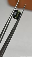 Cushion-cut green sapphire held in tweezers, top view