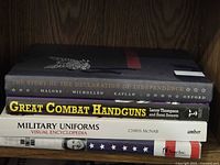Stack of four military history and weapons books on wooden shelf