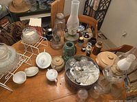 Overview of mixed glassware, oil lamps, teapot, flatware tin on dining table