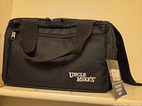 Front view of black Uncle Mike's range bag showing logo, zip pocket, handles and shoulder strap