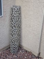 Full view of tall silver lattice metal column leaning against stucco wall on rock ground cover