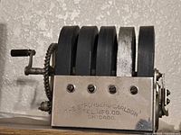 Right side view showing four black laminated core plates, hand crank, gear, nickel front plate with maker’s stamp
