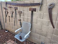 Wall display of long crosscut saw, curved saw, broad axe, assorted hatchets and pick head