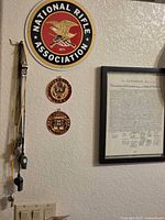Overall wall view showing NRA sign, two plaques, framed document, and whistles on lanyards