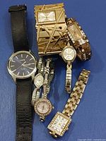 Group of seven assorted wristwatches laid on blue background, showing faces and straps