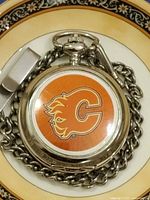 Closed pocket watch showing Calgary Flames logo on lid with chain and clip visible
