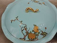 Close-up of serving dish lid showing turquoise glaze, chrysanthemum design, gold handle