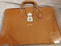 Front view of tan cowhide attaché briefcase showing handle, lock, monogram