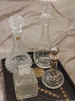 Four decanters grouped: round cut-crystal, clear glass carafe, square whiskey decanter, silver-overlay round decanter