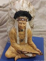 Front view of ceramic Indigenous chief statue with peace pipe and feather headdress