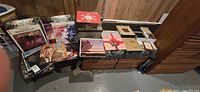 Overall lot view with Bible cassette binders, multiple LP records, boxes of ornaments, linens underneath