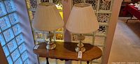 Front view of both matching brass and glass table lamps on small table