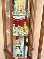 Glass display cabinet showing multiple Holly Hobbie porcelain figurines on three shelves