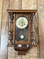 Full view of wall clock showing wooden case, columns, glass door, dial and pendulum